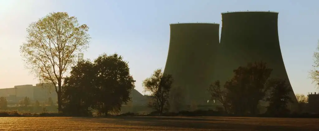 Les silhouettes de deux grandes tours de refroidissement se dressent au milieu des arbres et des terrains découverts dans la France nucléaire, avec le soleil bas dans le ciel, projetant une douce lueur sur la scène.
