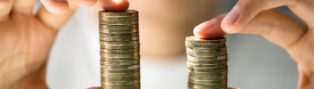 Deux mains tenant des piles de pièces de monnaie, l’une plus haute que l’autre, sur un arrière-plan flou, symbolisent la nécessité de comparer les coûts d’électricité pour réaliser des économies.