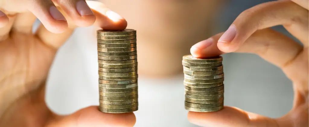 Deux mains tenant des piles de pièces de monnaie, l’une plus haute que l’autre, sur un arrière-plan flou, symbolisent la nécessité de comparer les coûts d’électricité pour réaliser des économies.