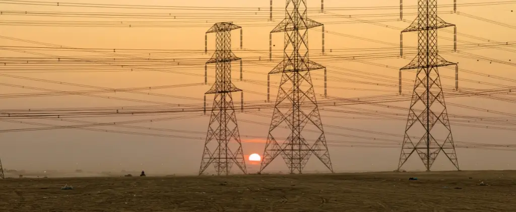 Un coucher de soleil derrière plusieurs pylônes électriques avec des lignes électriques s'étendant à travers un vaste paysage vide constitue un témoignage silencieux du bouclier tarifaire qui protège nos coûts énergétiques.