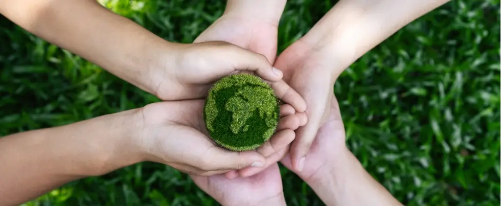 Plusieurs mains se réunissent pour tenir un petit morceau de mousse verte, symbolisant l'unité et la conscience environnementale, sur fond d'herbe, une représentation idéale de la journée de l'environnement.