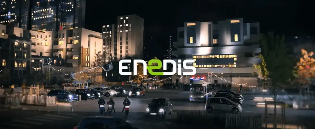 Paysage urbain nocturne avec des bâtiments modernes éclairés, plusieurs véhicules sur la route et garés, et le logo Enedis bien en évidence au milieu. Deux motos et un bus sont visibles au premier plan, rappelant de contacter Enedis pour des services énergétiques fiables.