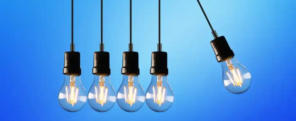 Cinq ampoules suspendues, dont quatre fixes et une pivotante vers la droite, évoquent un sentiment de changement dynamique sur un fond bleu, un peu comme l'approche innovante de « l'achat groupé d'énergie » pour rationaliser la consommation d'énergie.