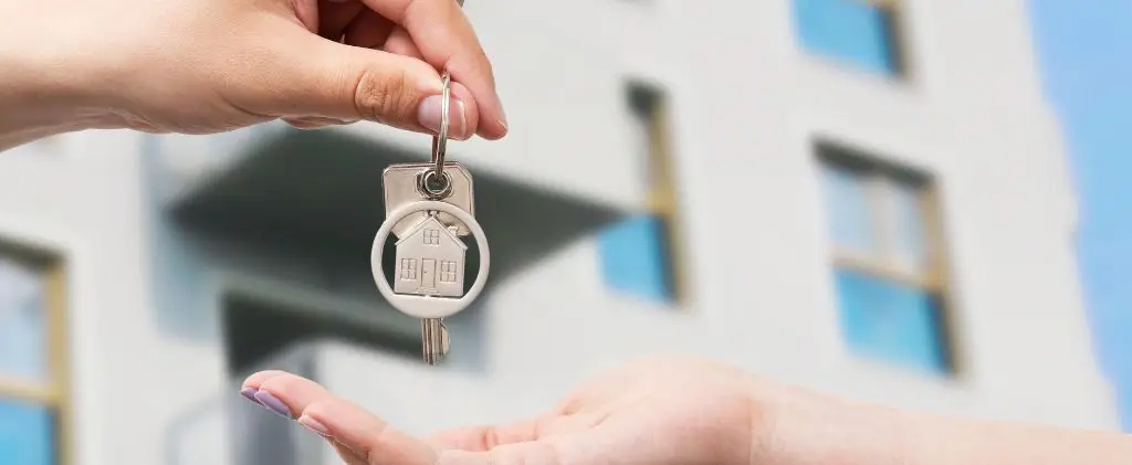 Une personne remettant une clé à une autre personne devant un immeuble indiquant le prix de référence du gaz pour les copropriétés.