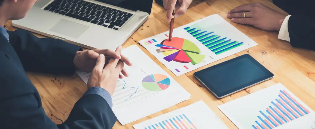 Professionnels d'affaires analysant des graphiques et des tableaux du marché de l'énergie avec un ordinateur portable et une tablette numérique sur une table en bois.