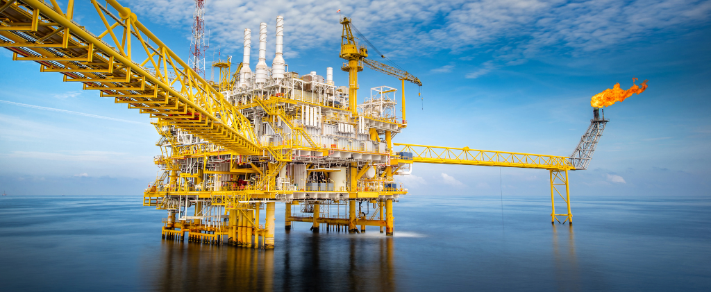 Une plate-forme pétrolière offshore se dresse dans l’océan sous un ciel bleu, avec une grande flamme brûlant au bout d’une structure étendue. Il y a aussi une grue visible sur la plate-forme principale, étiquetée ATRD7.