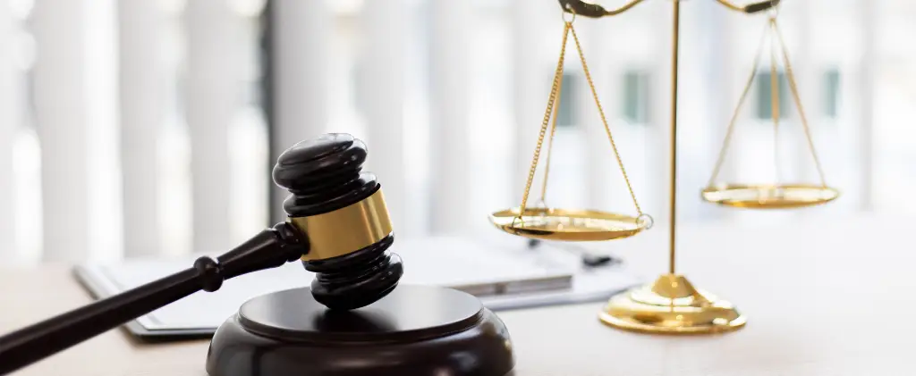 Un marteau de juge et une balance en laiton sont posés sur un bureau avec des documents de mise en service en arrière-plan.