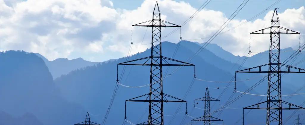 Des lignes électriques à haute tension avec des pylônes métalliques se dressent sur fond de montagnes et de ciel nuageux.