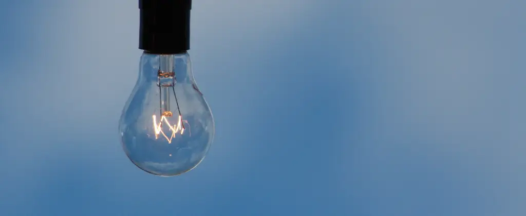 Une ampoule suspendue dans un ciel bleu clair, minimaliste et moderne pour évoquer les négociations post-ARENH en cours pour 2026.