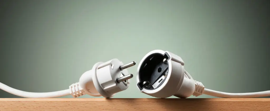 Une fiche et une prise électriques blanches, symbolisant un contrat d'électricité professionnel, sont déconnectées et reposent sur une surface en bois sur un fond vert.