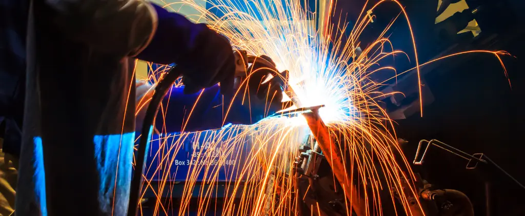 Un soudeur en tenue de protection, ressemblant à un fournisseur d'énergie pro, travaille sur du métal, créant des étincelles brillantes sur un fond sombre.