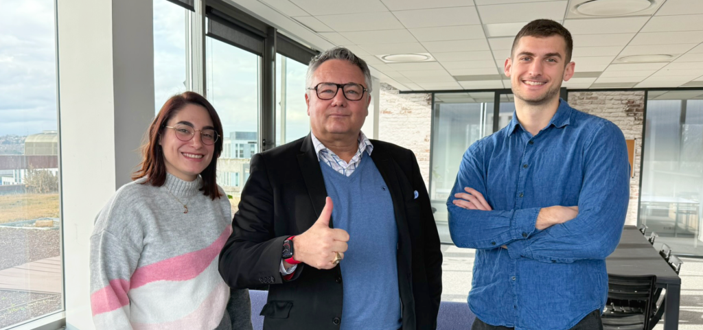 Trois personnes se tiennent à l'intérieur, deux sourient joyeusement et une lève le pouce, créant une atmosphère chaleureuse rappelant un showroom Meubles cosy.