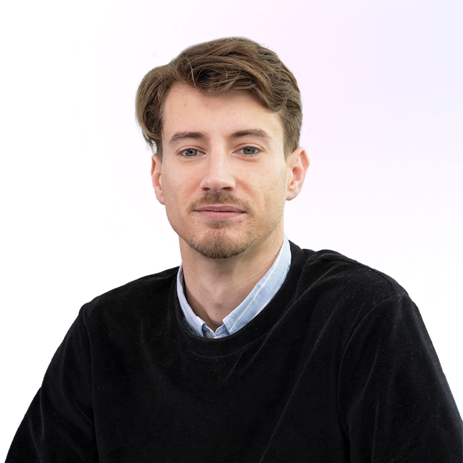 Une personne aux cheveux longs bruns portant un blazer bleu marine et un haut clair se tient debout avec confiance, souriant, les bras croisés, incarnant le professionnalisme de courtage en énergie TPE sur un fond blanc uni.