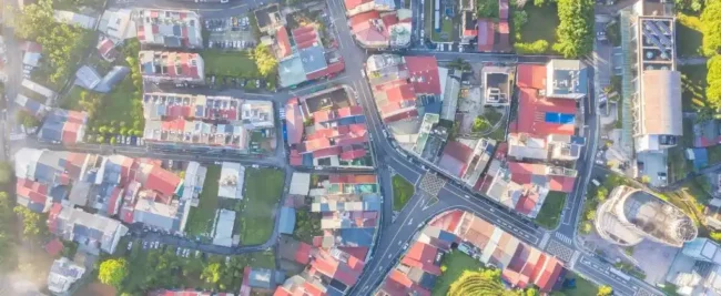 Vue aérienne d'une zone urbaine avec des routes qui se croisent, des zones herbeuses et de nombreux bâtiments aux toits colorés.