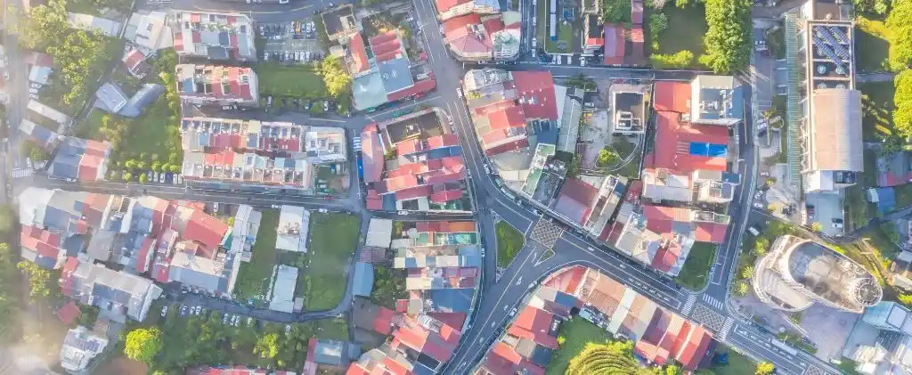 Vue aérienne d'une zone urbaine avec des routes qui se croisent, des zones herbeuses et de nombreux bâtiments aux toits colorés.