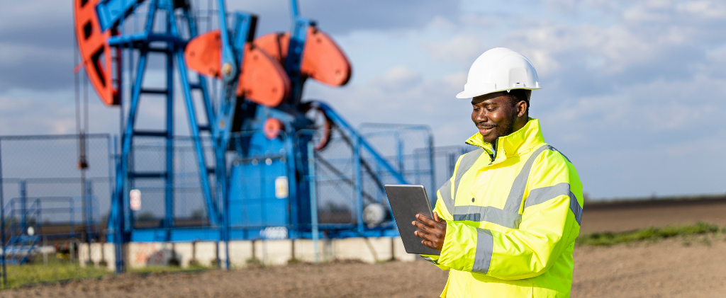 Un ingénieur en tenue réfléchissante et casque de sécurité examine l'évolution des tarifs de transport et de stockage du gaz sur une tablette près d'une pompe à pétrole bleue et orange dans un champ tentaculaire.