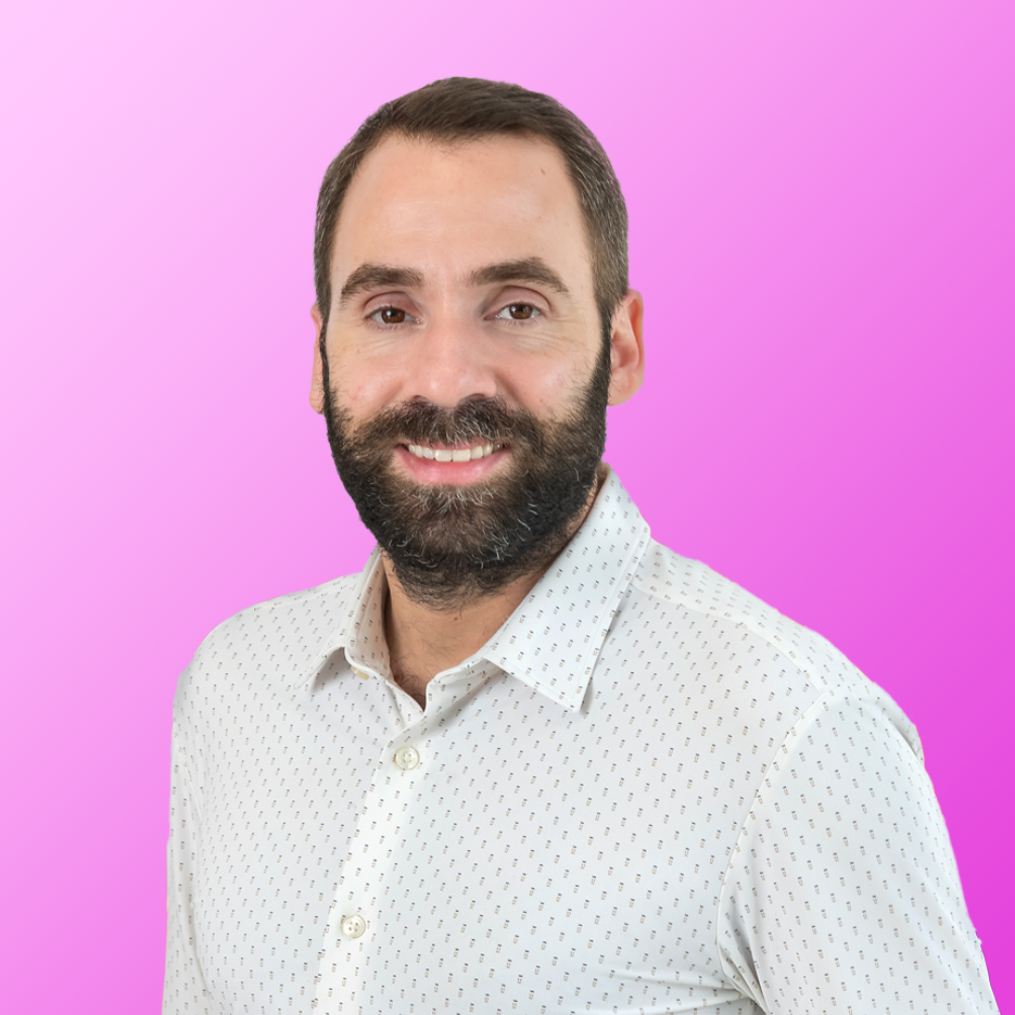 Un homme barbu vêtu d'une chemise blanche à motifs sourit avec assurance, incarnant l'esprit vibrant d'un événement marché public AMO, sur fond dégradé rose.