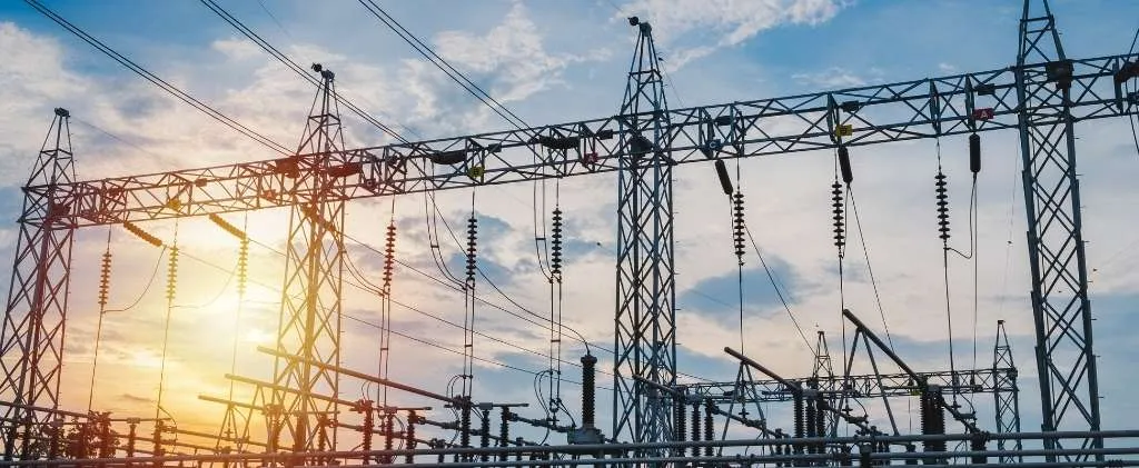 Un poste électrique, caractérisé par ses structures métalliques complexes et ses lignes électriques entrecroisées, se détache sur un ciel couchant, symbolisant la collaboration d'Enedis avec la collectivité pour garantir une circulation fluide de l'énergie dans nos communautés.