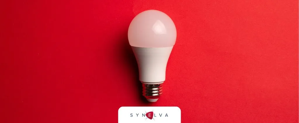 Ampoule LED sur fond rouge avec un logo « SYNEVA » en bas au centre, reflétant l'innovation et l'efficacité prônées par Primeo Energie.