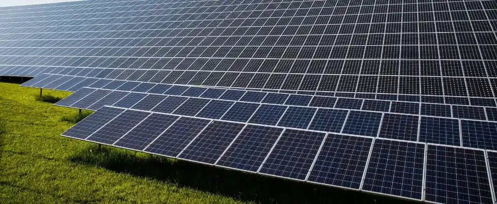 Des rangées de panneaux solaires sont installées à l'extérieur sur un terrain herbeux, positionnées pour capter la lumière du soleil afin de générer de l'énergie renouvelable, souvent dans le cadre de projets impliquant une définition PPA.