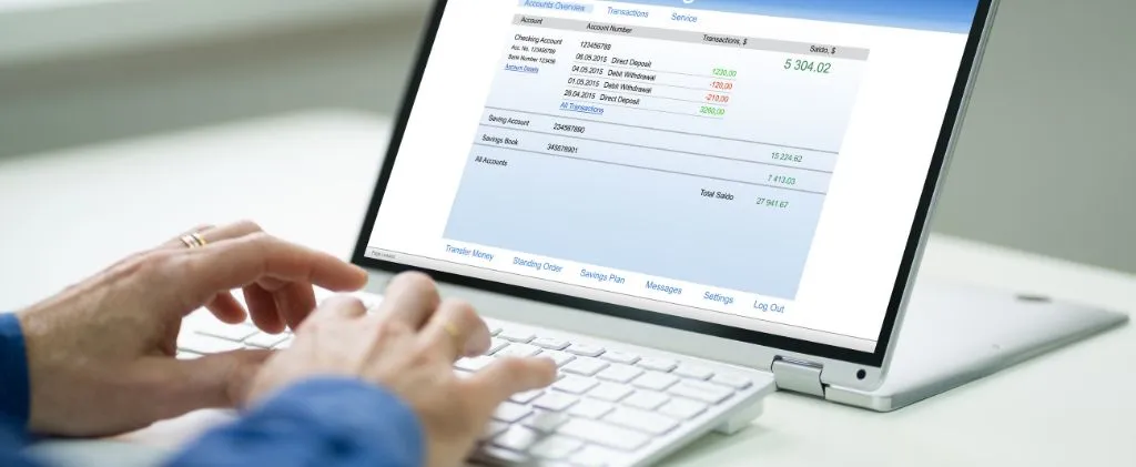 Des mains tapant sur un ordinateur portable affichant un écran de banque en ligne avec les détails des transactions et les soldes des comptes, reflétant peut-être les économies réalisées en choisissant l'électricité la moins chère.