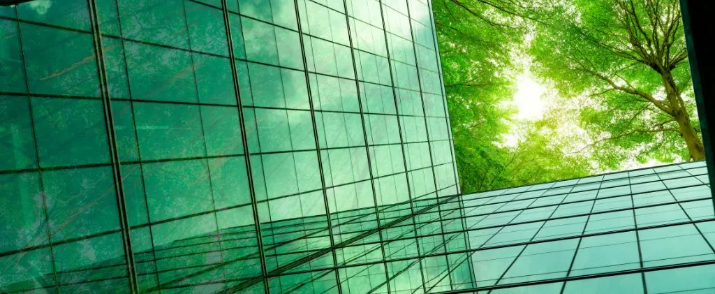 Le bâtiment en verre reflète les arbres verts, créant un mélange harmonieux d'architecture et de nature sous le ciel lumineux de Cee Avril 2025.