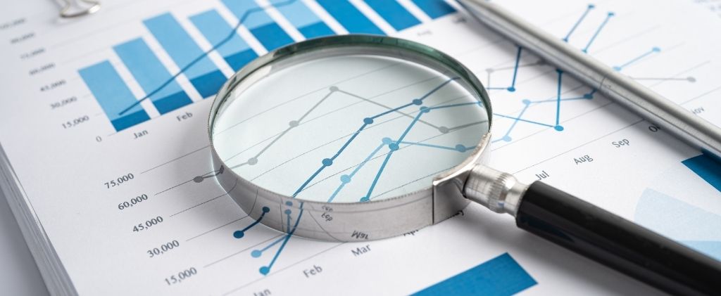 Une loupe posée sur des graphiques financiers à barres et à lignes, accompagnée d'un stylo, représentant des analyses de données et des rapports d'affaires pour les nouvelles offres Capitole Energie.