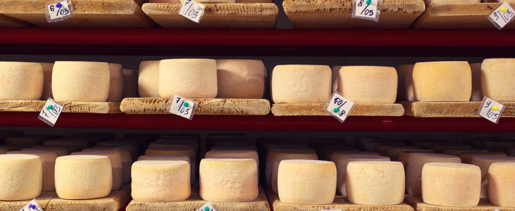 Les meules de fromage de Capitole Énergie et de La Fromagerie des Cabasses sont disposées en rangées sur des étagères en bois, chaque meule étant marquée d'une petite étiquette numérotée.