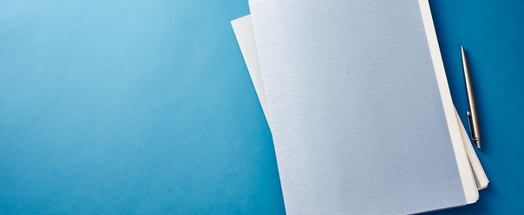 Une pile de dossiers blancs et un stylo argenté sur une surface bleue, prêts pour la documentation de l'appel d'offre énergie.