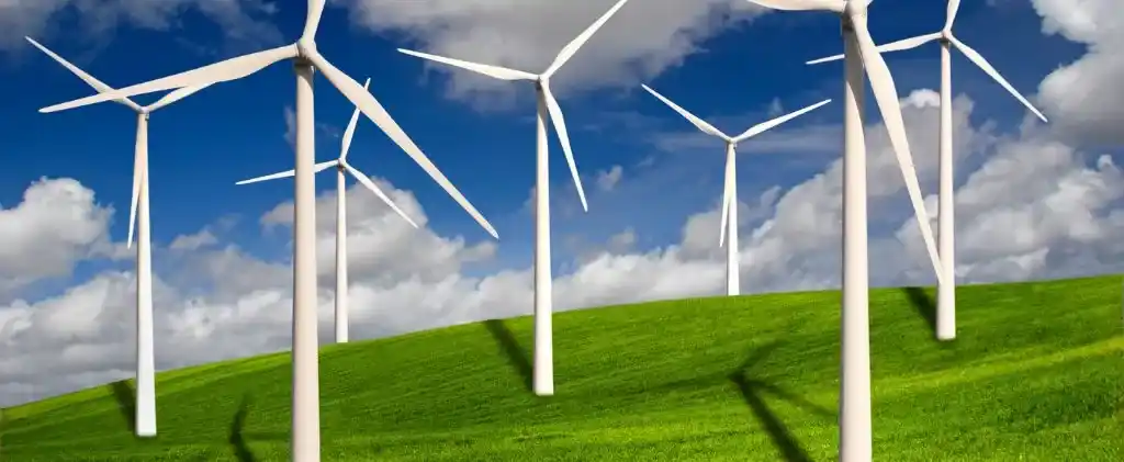 Plusieurs éoliennes blanches, faisant partie d'une entreprise de décarbonation, se dressent sur une colline herbeuse verte sous un ciel partiellement nuageux.