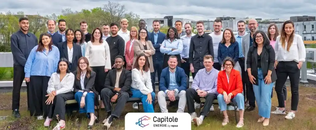 Un groupe de 30 personnes posant ensemble en extérieur devant un bâtiment, avec un panneau "Capitole ENERGIE" mettant en avant leur cabinet de conseil en énergie.