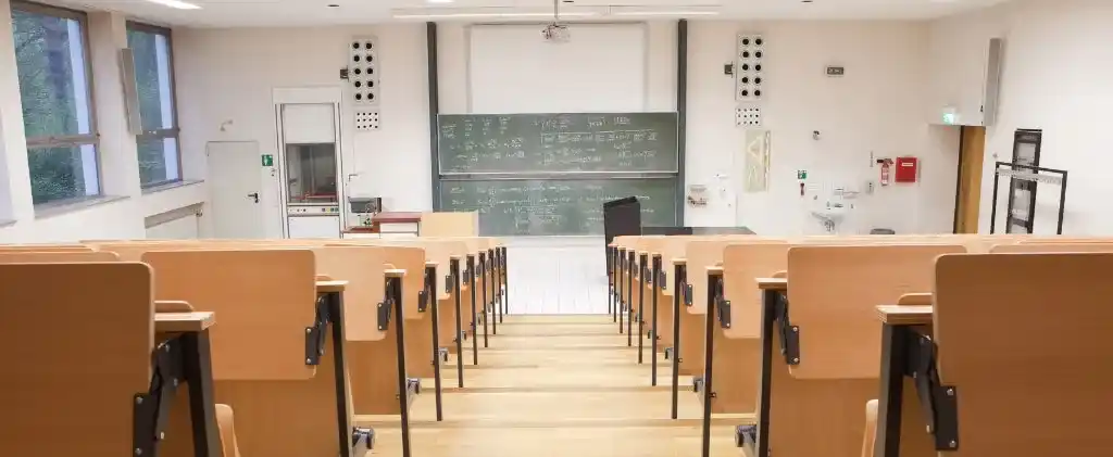Un amphithéâtre universitaire vide avec des sièges en bois, un tableau noir rempli d'écriture, un projecteur et divers équipements de classe à l'avant - idéal pour explorer l'optimisation énergétique dans les établissements scolaires.