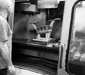 Une personne se tient à côté d'une fraiseuse CNC travaillant sur une grande pièce métallique dans un atelier industriel.