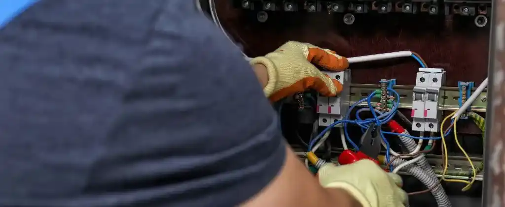 Une personne portant des gants travaille sur un panneau électrique, manipulant des fils et des disjoncteurs, tandis que divers outils sont visibles - soulignant l'importance de la sécurité et de la précision, en particulier lors d'un projet d'achat groupé énergie.