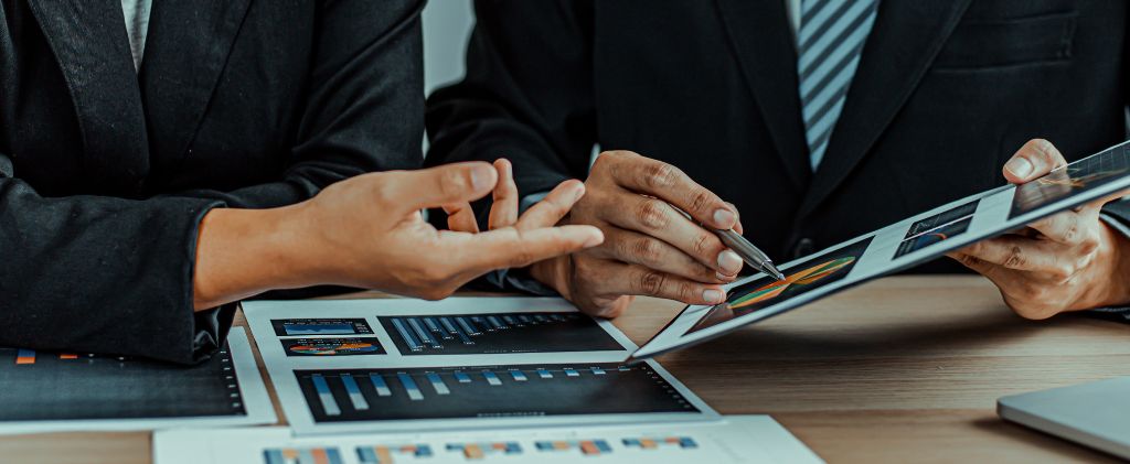Deux personnes en tenue de travail discutent de graphiques et de tableaux à un bureau, analysant les données d'un achat groupé d'énergie afin d'identifier les possibilités de réduction des coûts.