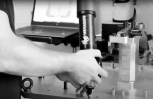 Une personne utilise un palpeur de mesure Hexagon sur un établi près d'un ordinateur portable et d'un équipement de précision dans un laboratoire ou un atelier.