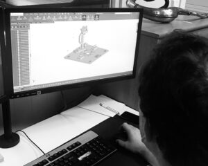 Une personne utilise un ordinateur avec un logiciel de CAO ouvert, affichant une conception mécanique en 3D sur l'écran.