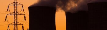 Tours de refroidissement d'une centrale électrique émettant de la vapeur au coucher du soleil avec une tour de transmission au premier plan, illustrant l'impact du mécanisme post arenh sur l'infrastructure électrique.