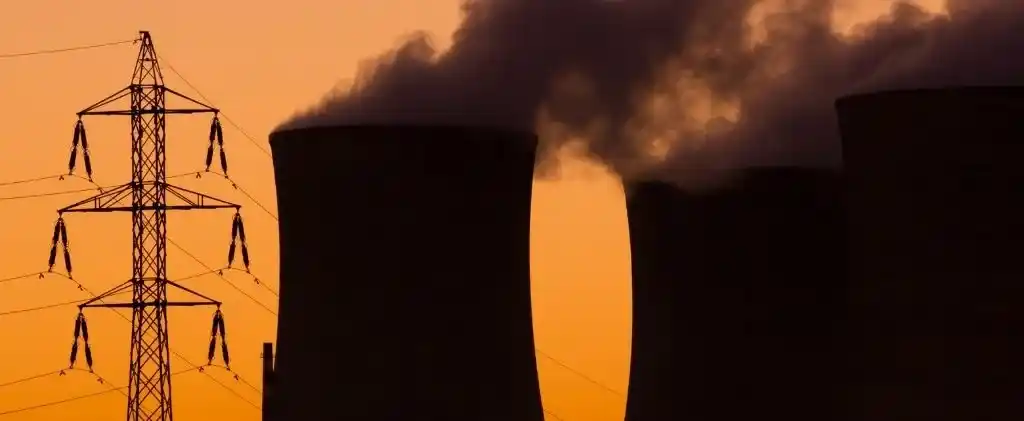 Tours de refroidissement d'une centrale électrique émettant de la vapeur au coucher du soleil avec une tour de transmission au premier plan, illustrant l'impact du mécanisme post arenh sur l'infrastructure électrique.