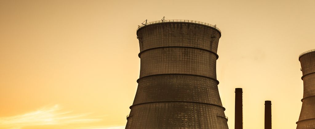 Deux grandes tours de refroidissement industrielles et deux cheminées se découpant sur un ciel jaune orangé évoquent l'atmosphère de la proposition de loi Gremillet sur la transition énergétique.