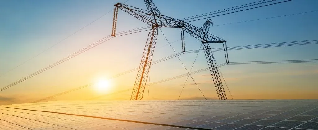 Des lignes à haute tension se dressent au-dessus d'un champ de panneaux solaires au coucher du soleil, illustrant les énergies renouvelables, le transport de l'électricité et le rôle des normes P6 CEE dans l'infrastructure moderne.