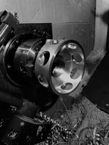 Un tour à métaux à commande numérique usine une pièce métallique cylindrique comportant plusieurs grandes découpes circulaires ; des copeaux de métal sont éparpillés autour de la zone de travail.