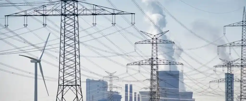 Des pylônes de transmission et des lignes électriques dominent le premier plan, tandis qu'une éolienne et une usine dégageant de la fumée sont visibles à l'arrière-plan, illustrant le paysage façonné par EDF et concurrence dans le secteur de l'énergie en pleine évolution.