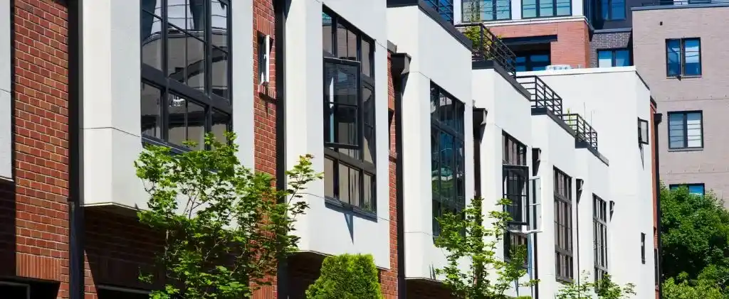 Une rangée de maisons de ville modernes avec de grandes fenêtres, des façades en briques et en blanc, et de petits arbres le long du trottoir, dispose d'un chauffage au gaz naturel efficace pour une vie citadine confortable.