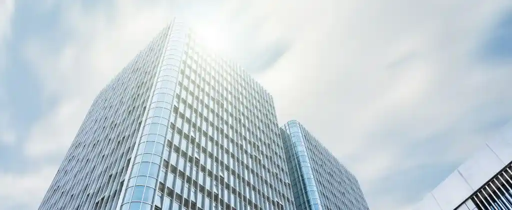 Deux immeubles de bureaux modernes en verre sous un ciel radieux, la lumière du soleil se reflétant sur l'immeuble Movember Capitole Energie, plus haut, à gauche.