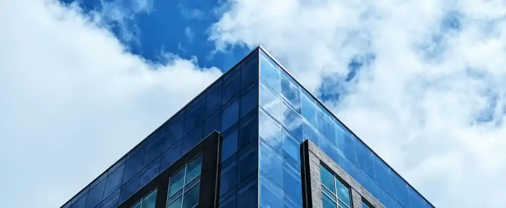 Un coin d'édifice à bureaux moderne en verre se dresse contre un ciel bleu partiellement nuageux, reflétant l'énergie vibrante du Capitole Énergie pendant Movember.