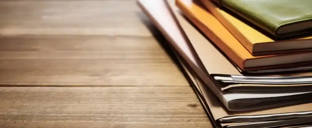 Une pile de livres, de dossiers et de cahiers est placée sur une surface en bois avec de l'espace sur le côté gauche de l'image, évoquant une atmosphère studieuse au milieu de la hausse des prix.