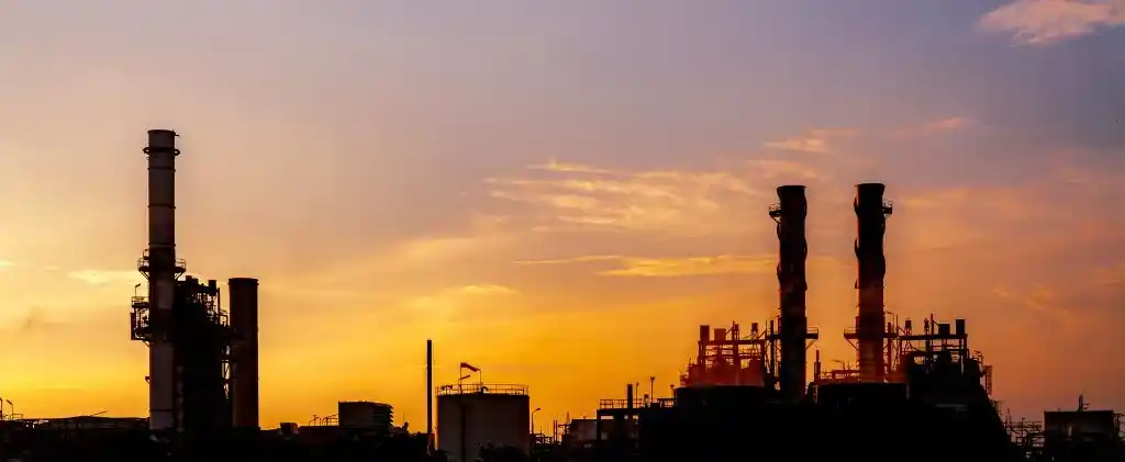 Silhouette de cheminées et de structures d'usines industrielles sur fond de ciel couchant orange et violet, évoquant les changements à venir dans le calendrier énergétique 2026.
