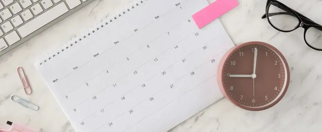 Un calendrier, une horloge, des lunettes et un clavier d'ordinateur sur un bureau blanc avec des trombones et une note autocollante rose - idéal pour planifier des tâches avec des échéances à prix fixe ou indexé.