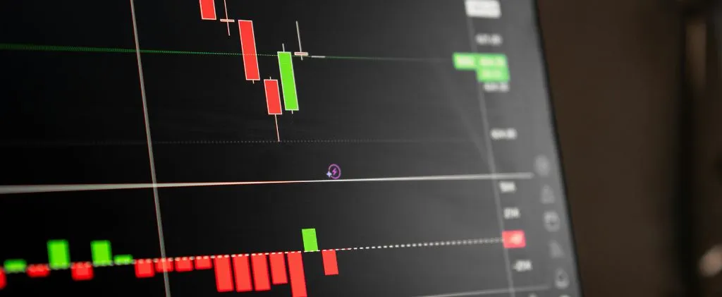 Un écran d'ordinateur affiche un graphique en chandeliers EJP avec des barres rouges et vertes, indiquant les mouvements de prix des actions ou des crypto-monnaies.